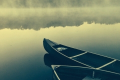 Two canoes wait ready by the shore of an early morning pond.